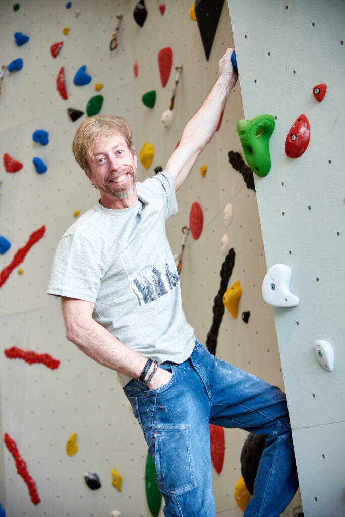 An image of Andreas Oliver Bindhammer, founder and CEO of eXXpozed, climbing and looking into the camera.