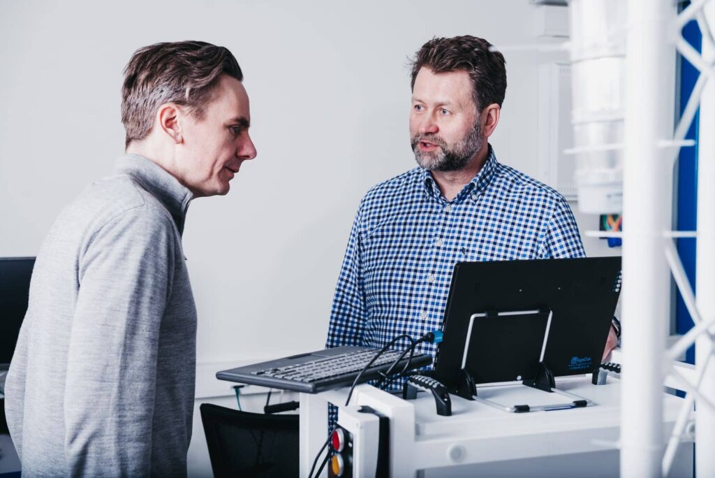 Two men standing by a computer and talking