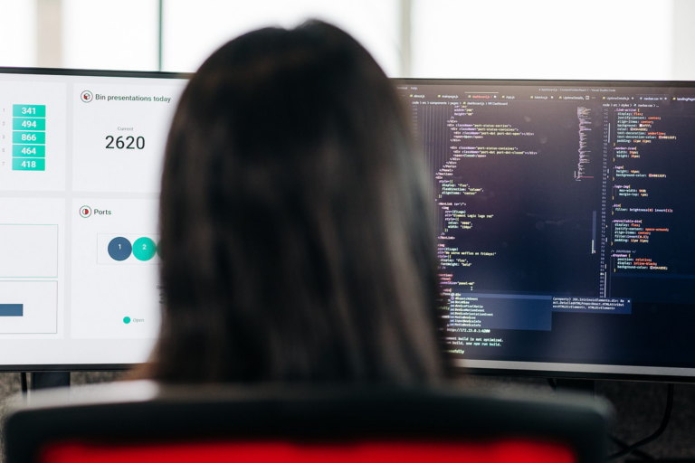 Woman looking at two screen with code and a dashboard