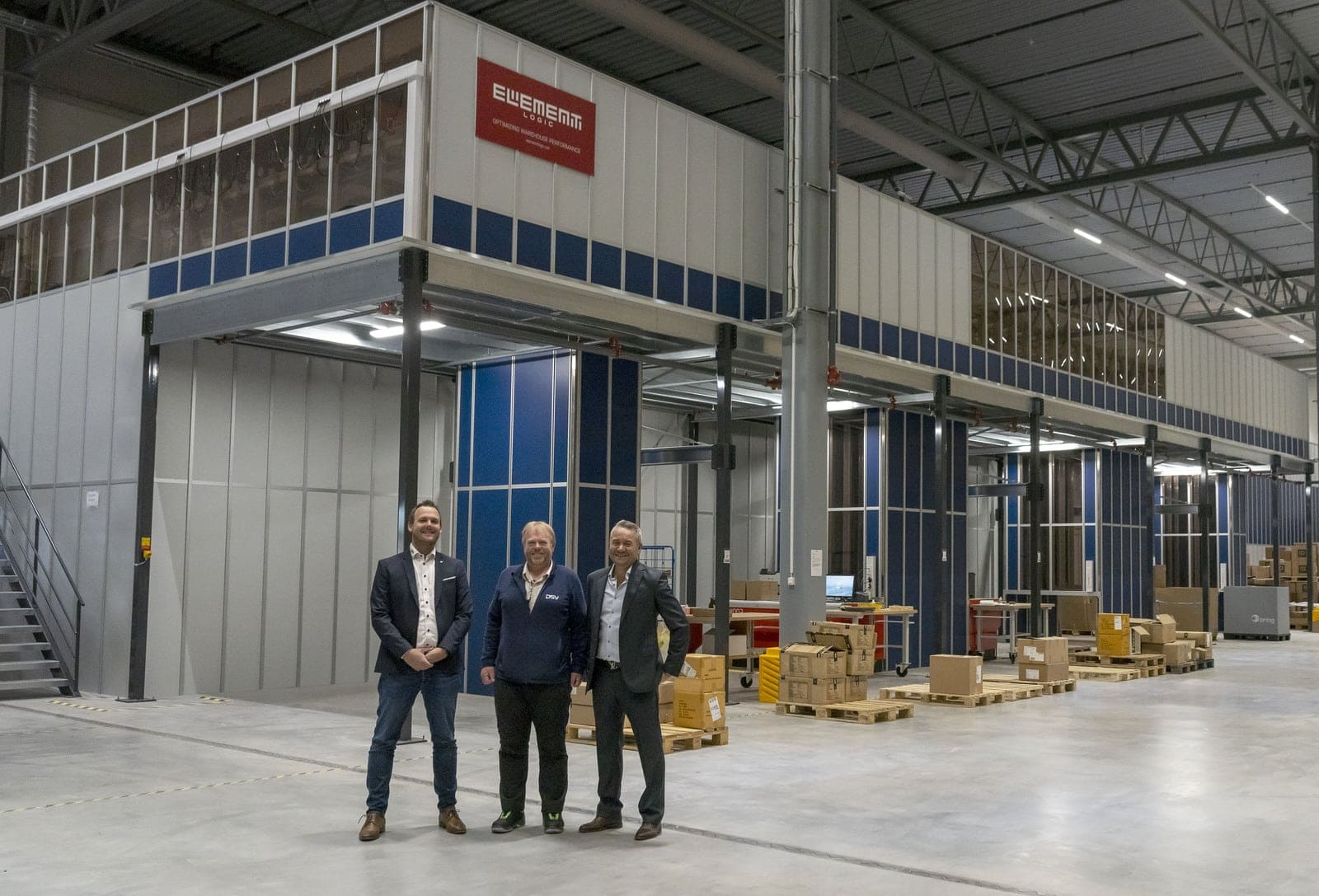 Three men in front of an automated warehouse