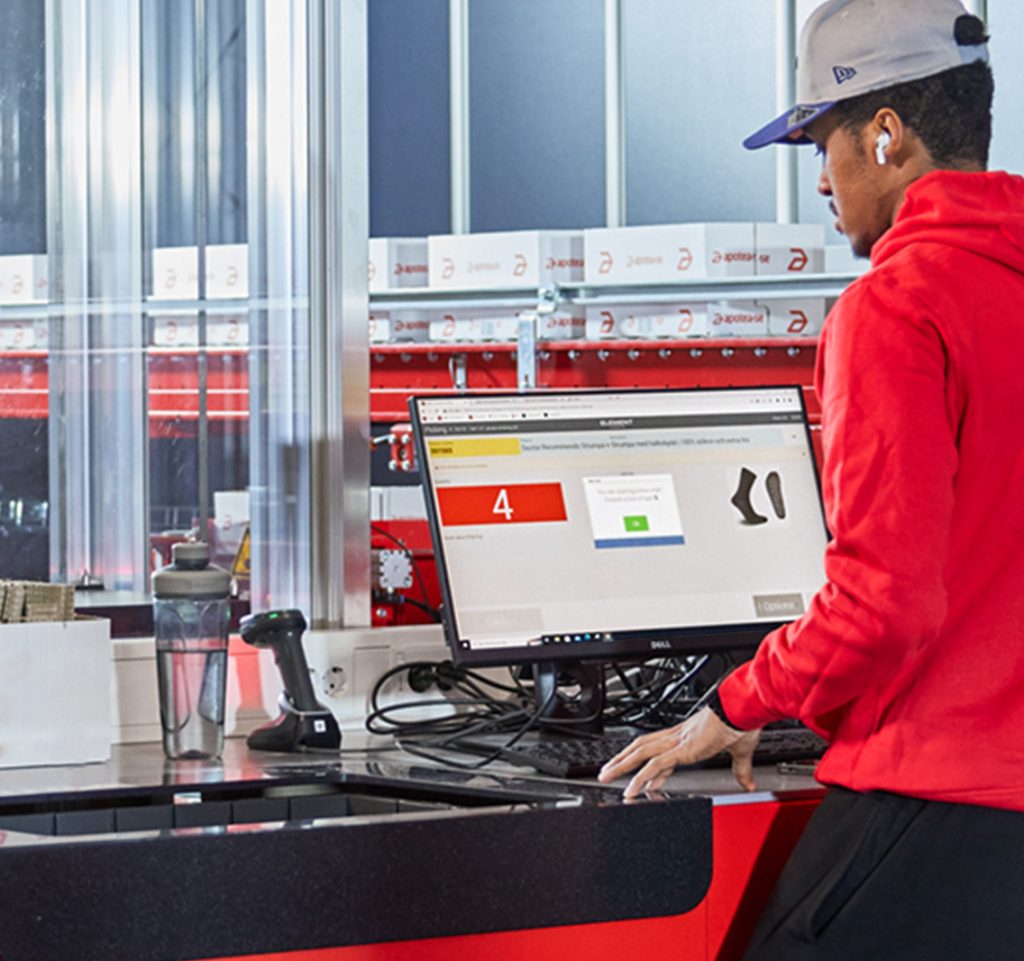 Operario con sudadera roja utiliza en una estación de trabajo de un sistema ASRS.