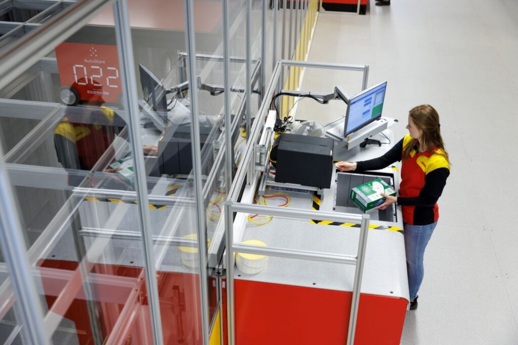 Operaria interactuando con una estación de trabajo AutoStore en un almacén automatizado.
