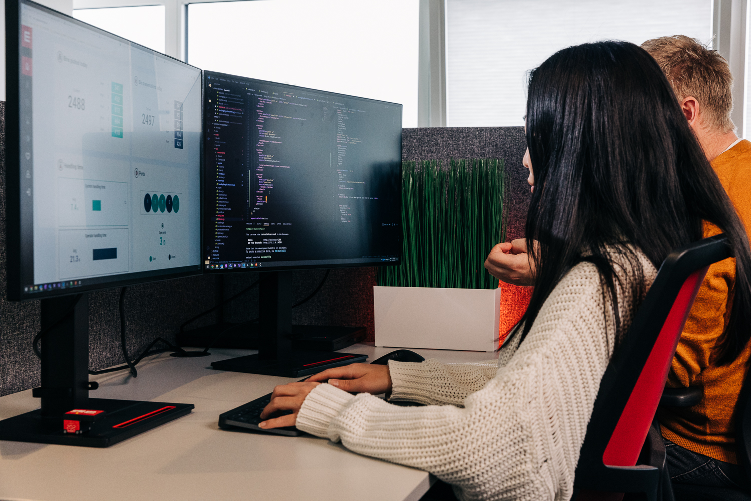 Dos profesionales de TI analizando datos de almacén en monitores duales en un entorno de oficina moderno.