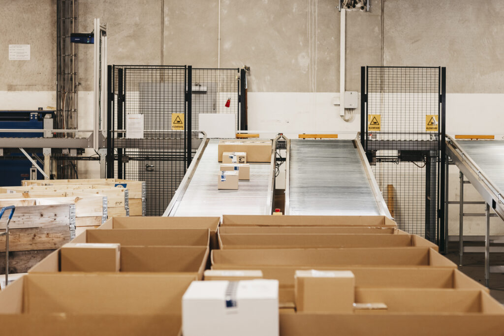 Interior de un almacén logístico mostrando una zona de transporte con cajas en cintas transportadoras y palets de madera en primer plano