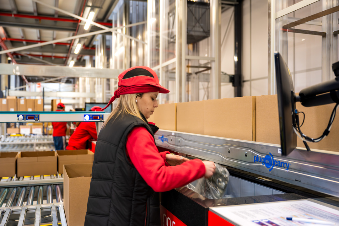 Operaria en una estación AutoStore manipulando productos para preparación de pedidos en un almacén automatizado.