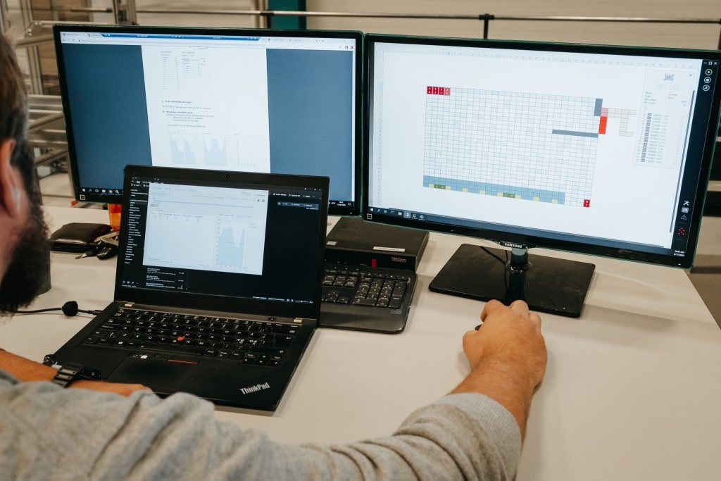 Un uomo sta lavorando alla soluzione AutoStore con tre schermi di computer.