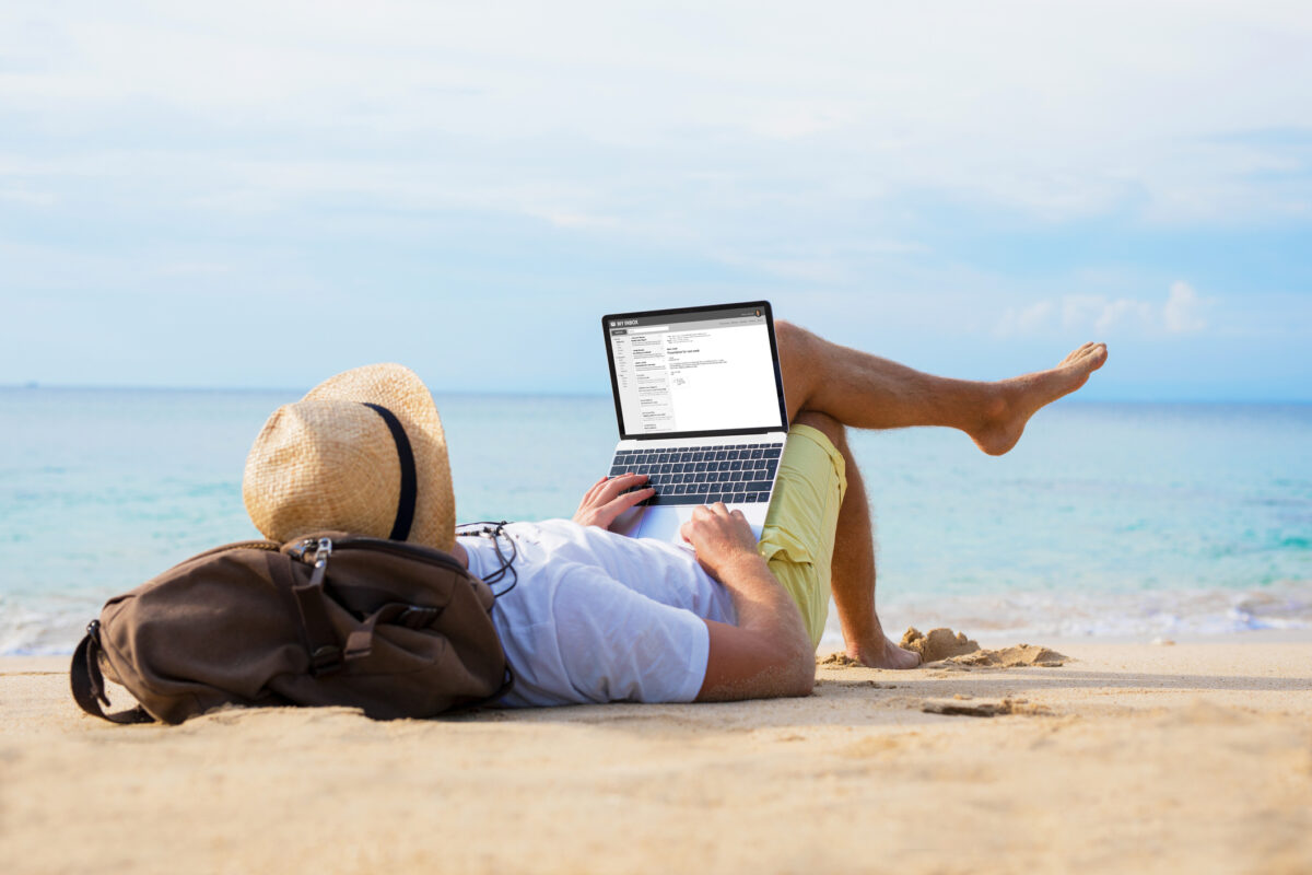 man laying down on the beach while working on a laptop.